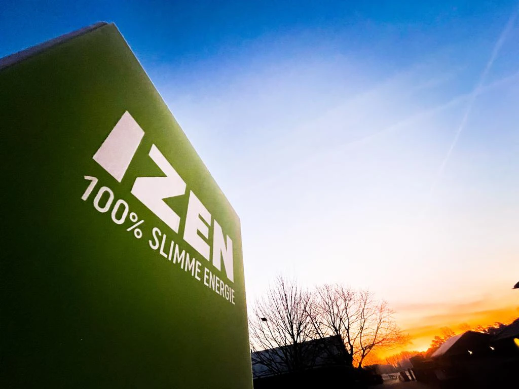 Een groen bord met in het wit het logo van IZEN bij de oprit van de kantoren van IZEN bij zonsopgang.